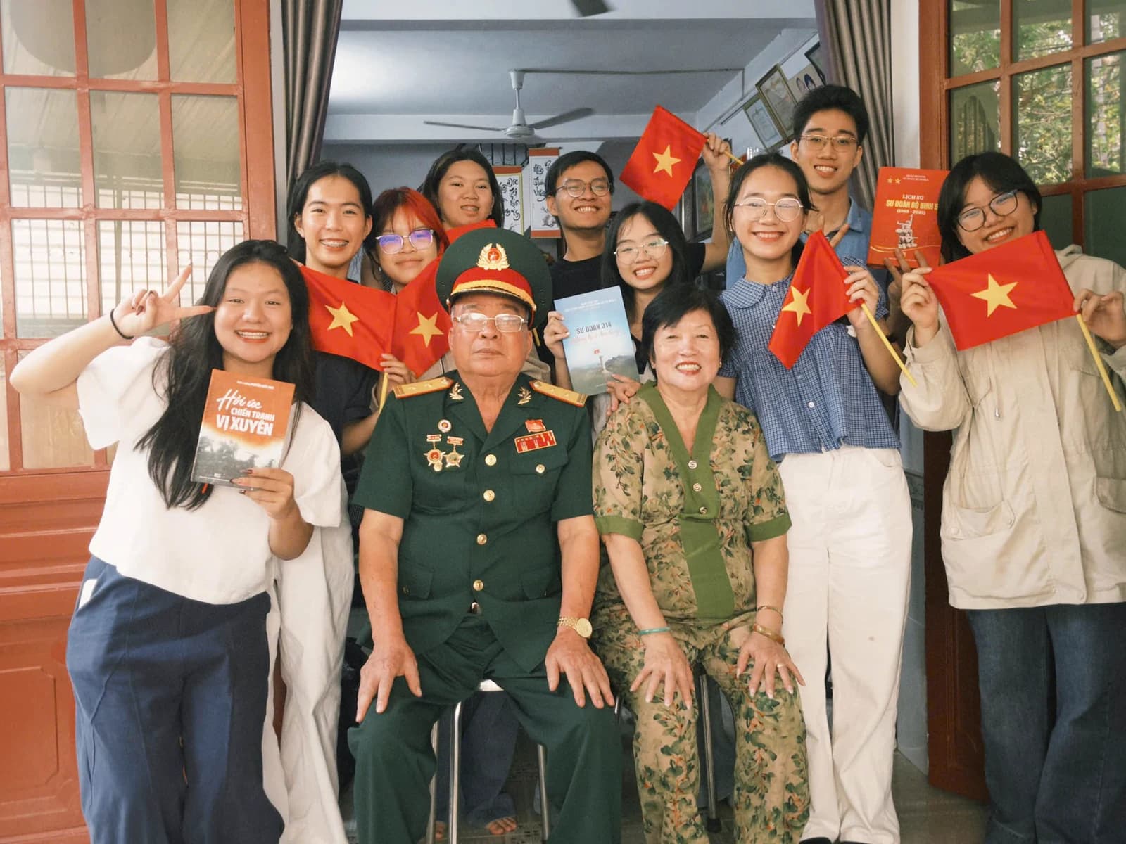A group of young people photographed with two veterans, holding Vietnamese flags.