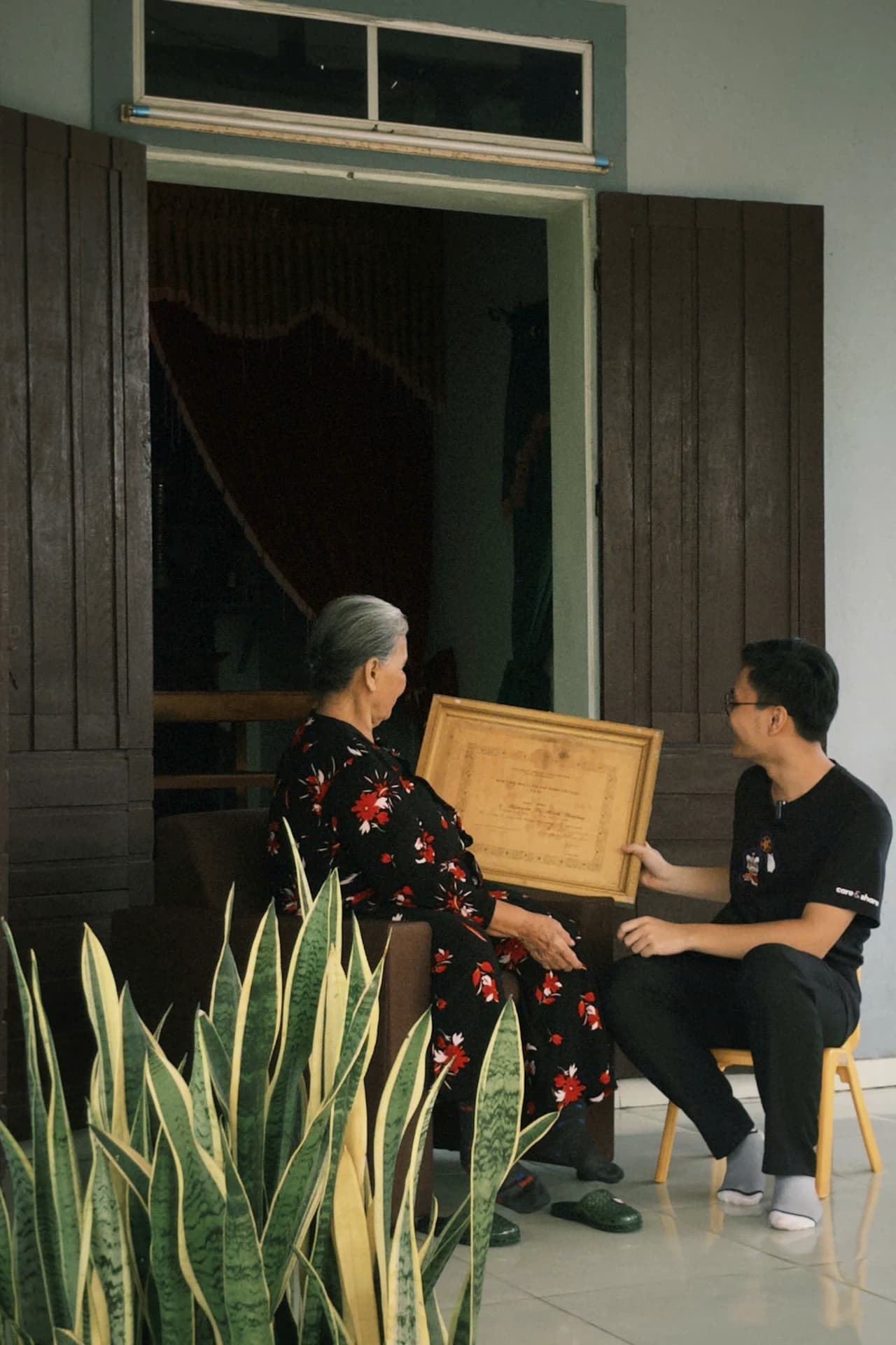 An older woman and a young man looking at a framed keepsake together.