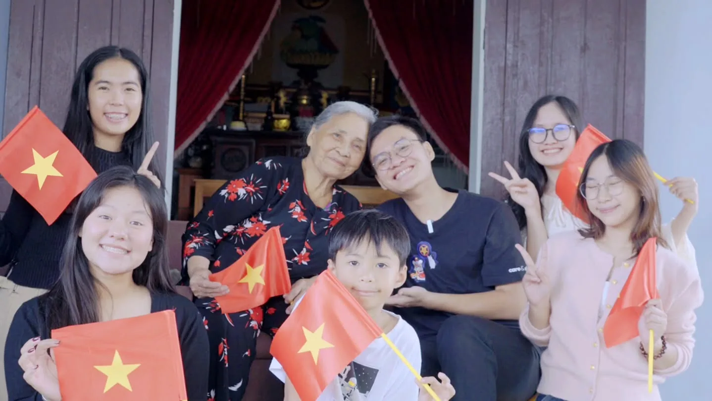 Ba thế hệ ngồi bên nhau, tay cầm cờ Tổ quốc.